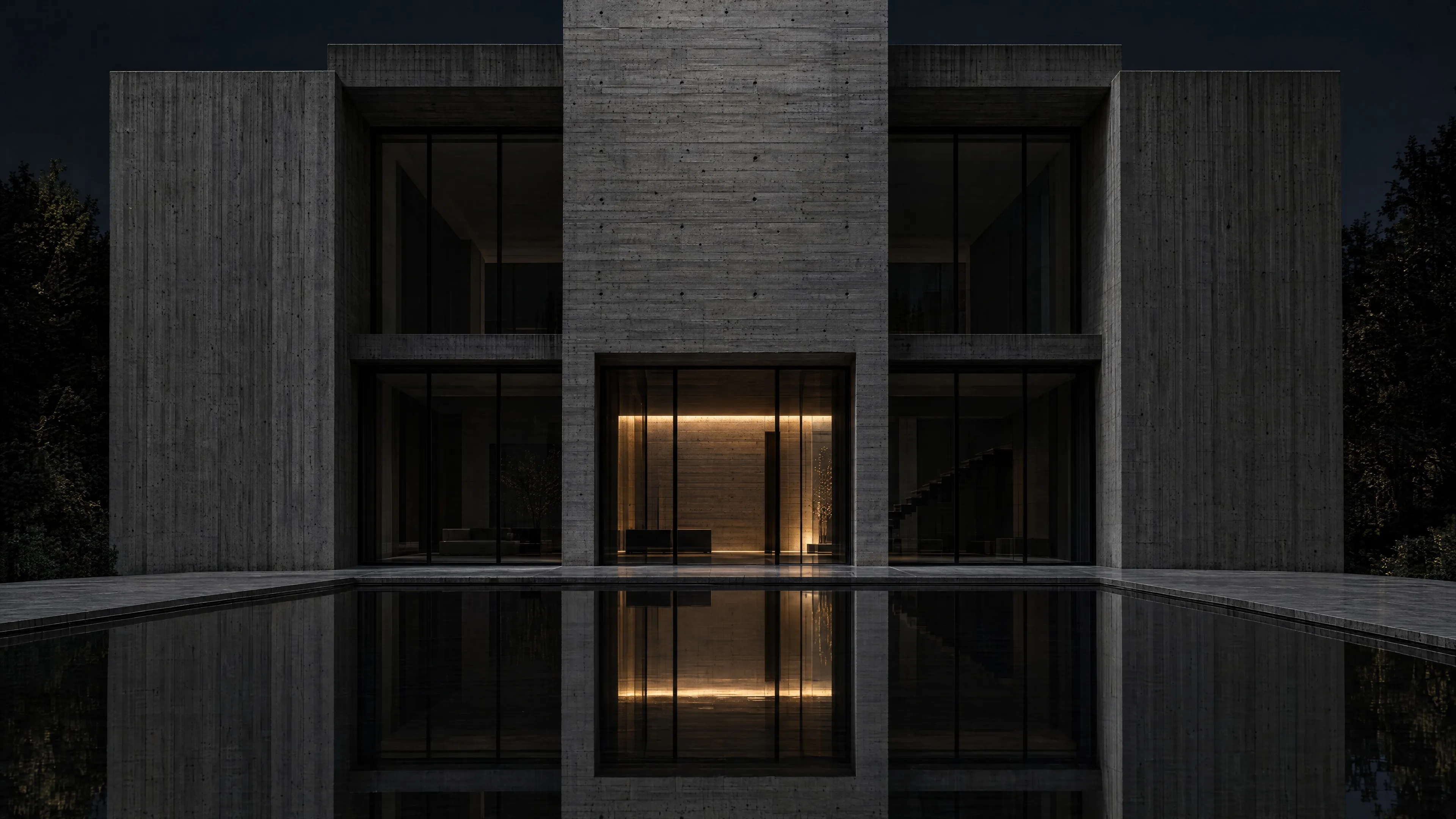 Monolithisches Gebäude aus Sichtbeton bei Nacht, ein Lichtband im Eingang spiegelt sich im Wasserbecken